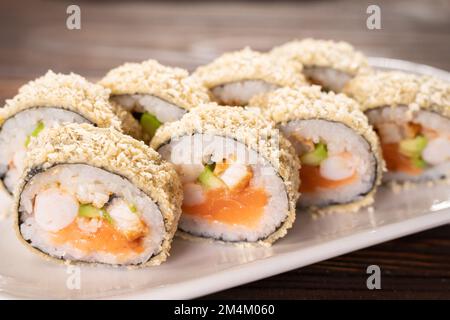 Rullo di sushi caldo alla tempura giapponese su piatto bianco su sfondo di legno. pezzi di sushi con salmone, formaggio cremoso, avocado avvolto in riso con crunchy seaw Foto Stock