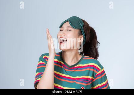 Ragazza che indossa una maschera verde che copre la bocca aperta con la mano che agisce sonnolenta su sfondo bianco. Foto Stock