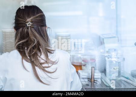 ritratto di una donna in un camice bianco, un ricercatore scientifico che sta facendo esperimenti in un ambiente asettico, persona irriconoscibile perché ha Foto Stock