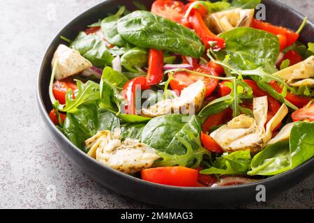 Insalata vegana di cuori di carciofi, pomodori ciliegini, spinaci, rucola, peperoni fritti e cipolle primo piano in un piatto sul tavolo. Orizzontale Foto Stock