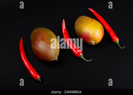 Mango interi e peperoncino su sfondo nero. Ingredienti per chutney di mango piccante. Foto Stock