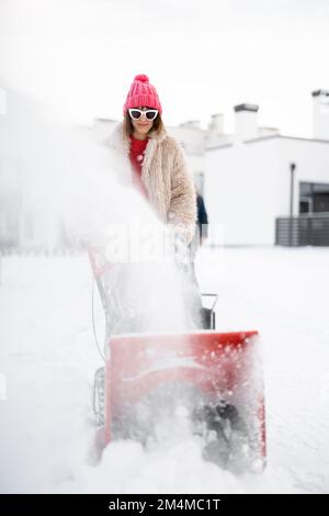 Donna rimuove la neve dal percorso con una macchina spazzaneve Foto Stock