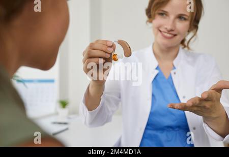 Un audiologo sorridente offre un moderno apparecchio acustico a un paziente minorenne con problemi di udito Foto Stock