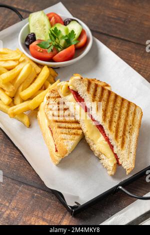 Toast con formaggio cheddar e salsiccia turca con patatine fritte e insalata su tavola di legno Foto Stock