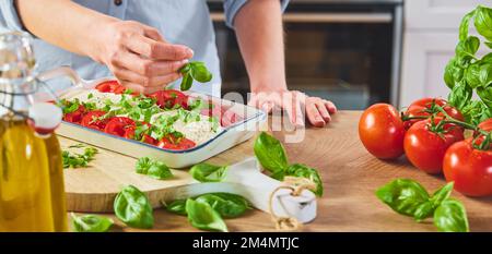 Alto angolo di raccolto Unriconoscibile cuoca femmina in piedi vicino al banco di legno e decorazione caprese con foglia di basilico posto sul tagliere di legno vicino Foto Stock