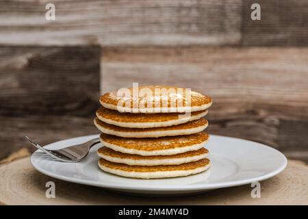 Una grande pila di frittelle con una forchetta contro un fondo di legno semplice senza sciroppo Foto Stock
