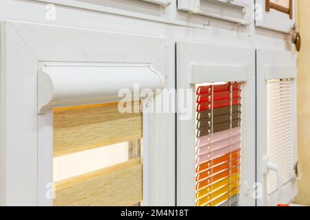 Campioni di tende per finestre nel negozio. Tende in plastica, tende pieghettate, avvolgibili e tende diurne e notturne in negozio. Foto Stock