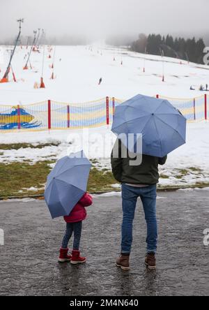 22 dicembre 2022, Sassonia, Oberwiesenthal: Due vacanzieri con ombrelloni si trovano sotto la pioggia sulla pista sciistica di Fichtelberg. Solo pochi giorni dopo l'inizio, la stagione sciistica in Sassonia è minacciata di una pausa più lunga. Sul Fichtelberg, un solo ascensore era aperto lo stesso giorno. Se continua a piovere così, le operazioni saranno sospese da venerdì (23,12.). Precipitazioni e vento stanno mettendo una tensione sulla copertura di neve sulle piste. Secondo il servizio meteorologico tedesco, rimarrà piovoso nei giorni di Natale con temperature fino a dieci gradi, e anche in montagna è ex Foto Stock