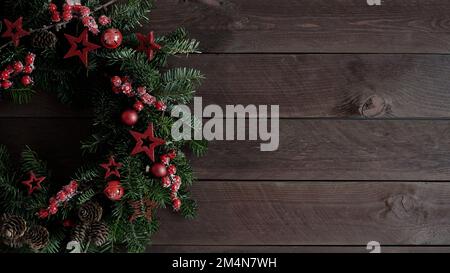 Primo piano della bella corona di Natale alberi di Natale pazzo naturale decorato con stelle, coni e bacche si trova su vecchie tavole di legno scuro, vista dall'alto, copia Foto Stock