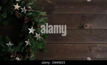 Primo piano della bella corona di Natale alberi di Natale pazzo naturale decorato con stelle, coni e bacche si trova su vecchie tavole di legno scuro, vista dall'alto, copia Foto Stock