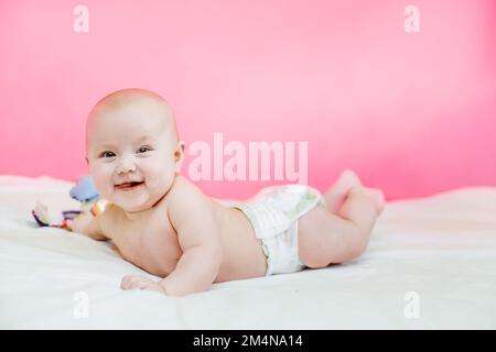 il bambino si trova sul pancino del letto con le gambe sollevate. Adorabile bambino in camera bianca soleggiata. Bambino neonato che si rilassa nel letto che si distenderà sullo stomaco Foto Stock