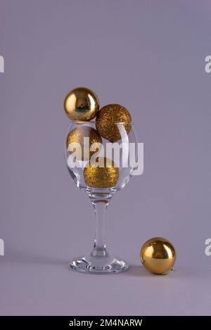 palline d'oro di natale in un bicchiere di vino su sfondo grigio Foto Stock