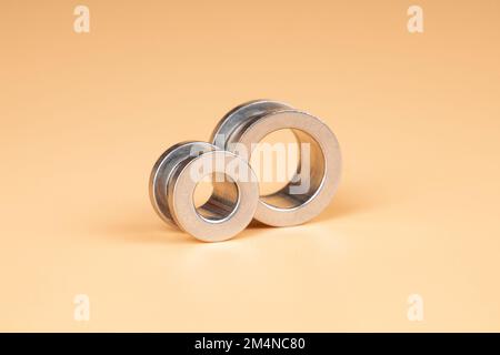 accessorio piercing tunnel d'argento primo piano su sfondo beige. Foto Stock