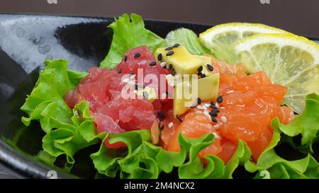 Un primo piano di una tartara di tonno salmone servito su un piatto nero Foto Stock