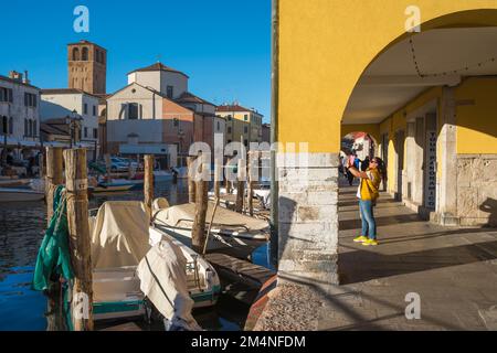Fotografia di viaggio donna, vista di una donna in piedi in un colorato colonnato a Chioggia e scattare una foto di un canale panoramico, comune di Venezia, Italia Foto Stock
