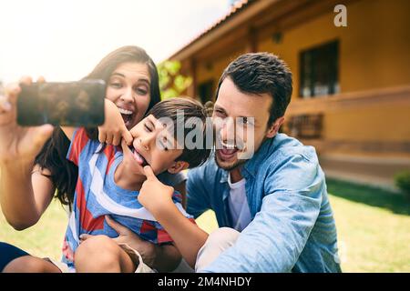 Fare ricordi. una giovane famiglia felice di tre selfie bianco seduto nel cortile. Foto Stock