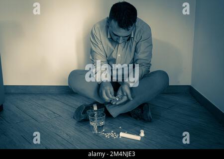 Immagine di un uomo disperato seduto a terra che abusa di pillole. Abuso di droga e droga e problema di dipendenza. Foto Stock