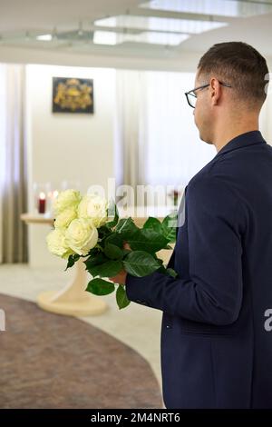 Olaine, Lettonia - 17 novembre 2022: L'uomo in giacca scura tiene un bouquet di rosa bianca fresca. Vista dal retro. Concetto di celebrazione. Foto Stock