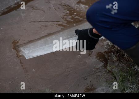 Un ragazzo adolescente rimuove un pezzo di ghiaccio spesso da un lago ghiacciato durante il recente clima freddo nella nuova foresta Hampshire Regno Unito. Foto Stock