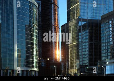 Grattacieli di edifici densi in piedi nell'area degli affari con riflesso del sole in serata in primo piano con vista frontale del tramonto Foto Stock