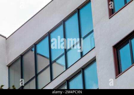 Pareti bianche con grandi finestre riflettenti blu. Moderno edificio residenziale facciata dettagli architettonici. Elementi di design per esterni immobiliari Foto Stock