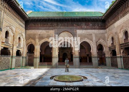 Cortile interno con bacino d'acqua, visitatori fotografando facciate in legno e portici, ornamenti, 14th ° secolo college islamico, Medersa Bou Inania, Fes Foto Stock