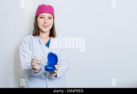 Un dentista con fermi su sfondo isolato, Ritratto di sorridente dentista con fermi dentali isolato. Giovane dentista sorridente che ne mostra alcuni Foto Stock