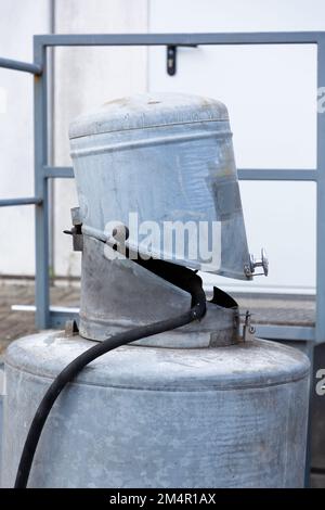 Un piccolo contenitore rotondo in metallo è montato su un contenitore più grande. Quello più piccolo è aperto come una bocca con un tubo che conduce fuori da esso. Foto Stock