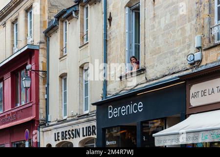 Donna che guarda fuori dalla finestra su Rue Saint Martin nel centro di Bayeaux, Francia Foto Stock