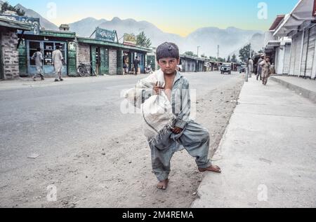 Pakistan, Peshawar - 30 giugno 1987: Ragazzo che porta un sacco di riso nella strada principale di Peshawar, Pakistan. Foto Stock