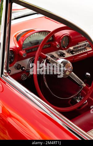 Il volante e il cruscotto di una Ford Thunderbird rossa del 1955 visti attraverso una finestra aperta. Foto Stock