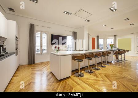 Una grande isola centrale piena di sgabelli di legno e metallo in una cucina con pavimenti in legno massiccio tinto pino Foto Stock