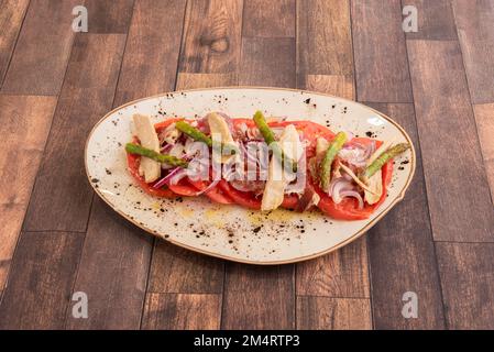 Tradizionale insalata spagnola di tonno alla pancia con abbondante cipolla rossa, fette di pomodoro, olio d'oliva e sale e asparagi selvatici Foto Stock