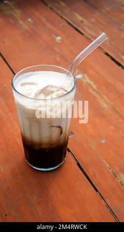 Cappuccino ghiacciato in un alto bicchiere trasparente servito su un tavolo di legno marrone con una foto ritratto scattata Foto Stock