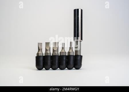 Set di utensili per bullonatura in metallo di varie dimensioni. Diversi tipi di punte per cacciaviti. Pila di strumenti metallici sostituibili su sfondo bianco sfocato Foto Stock