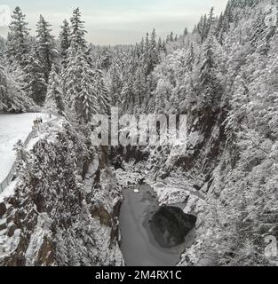 Guardando verso il basso nell'abisso della diga di Cleveland e il ghiacciato fiume Capilano circondato dal paesaggio invernale innevato a North Vancouver, BC, Canada Foto Stock