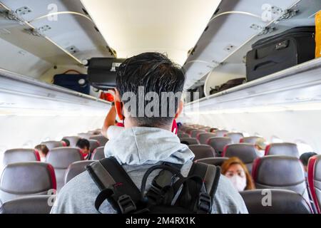 I passeggeri camminano nella cabina di un aereo. un uomo asiatico che cammina lungo la navata della cabina dell'aereo Foto Stock