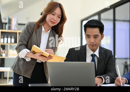 Attraente giovane segretaria asiatica o assistente che lavora con il suo capo maschio in ufficio. Foto Stock