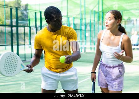 Allenatore di padel uomo che insegna alla giovane donna di servire la palla Foto Stock