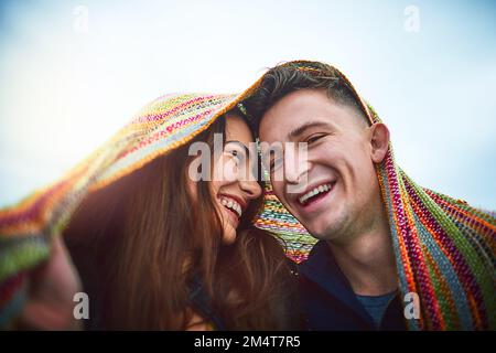 Innamorati. una giovane coppia felice che si copre con una coperta all'aperto. Foto Stock