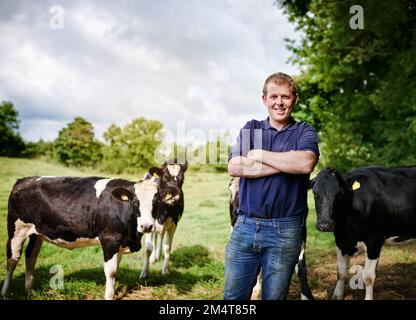 Casa è dove sono le mie mucche. Ritratto di un agricoltore maschio in piedi con le braccia ripiegate sulla sua azienda casearia. Foto Stock