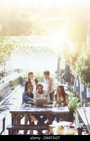 Un altro esempio di come la tecnologia riunisca le persone. un team di colleghi che utilizza un computer portatile insieme durante una riunione in un bar all'aperto. Foto Stock