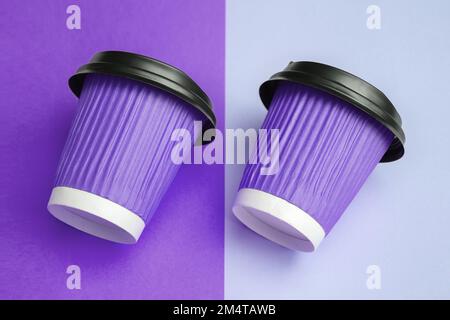 Immagine ravvicinata di due tazze di carta viola per caffè o tè da asporto disposte parallele e inclinate a destra su un colorato tavolo di design. Spazio di copia. Messa a fuoco selettiva morbida Foto Stock