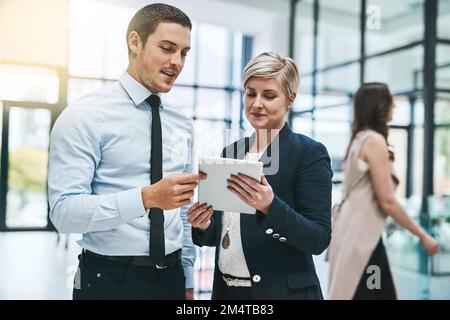 Ottenere una seconda opinione. due giovani uomini d'affari che lavorano su un tablet digitale in un ufficio impegnato. Foto Stock