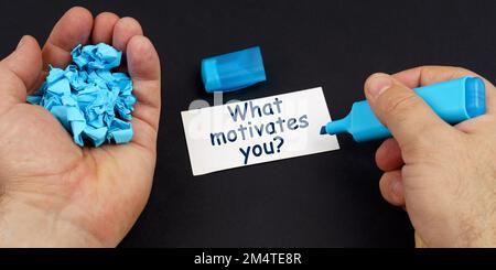 Concetto aziendale. Nelle mani di un uomo è di carta stropicciata blu e un marcatore, su una tabella nera è un biglietto da visita con l'iscrizione - che cosa motiva Foto Stock