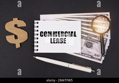 Concetto di business e finanza. Su una superficie nera si trovano i dollari, un simbolo, una lente d'ingrandimento, una penna e un blocco note con l'iscrizione - LEAS COMMERCIALE Foto Stock