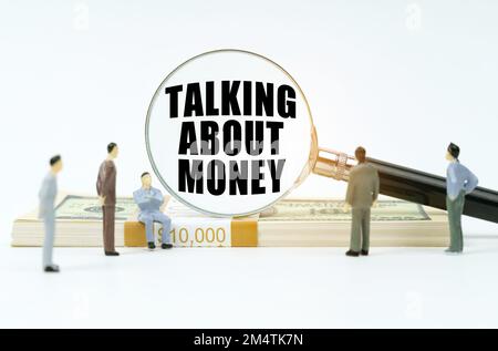 Economia e finanza. Su sfondo bianco, monete, un pacco di dollari, figure di uomini d'affari che guardano una lente d'ingrandimento con gli inscripti Foto Stock