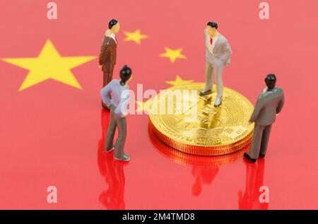 Criptovaluta e concetto di business. Sulla superficie con l'immagine della bandiera della Cina sono bitcoins e figurine in miniatura della gente. Foto Stock