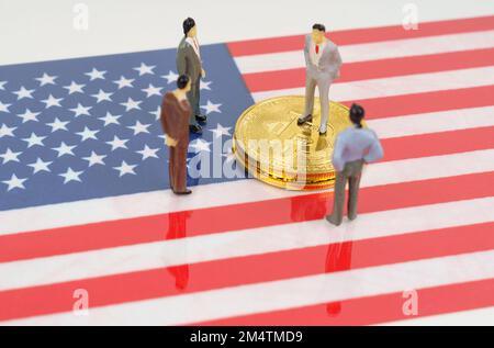 Criptovaluta e concetto di business. Sulla superficie con l'immagine della bandiera degli Stati Uniti ci sono bitcoins e figure in miniatura di persone. Foto Stock