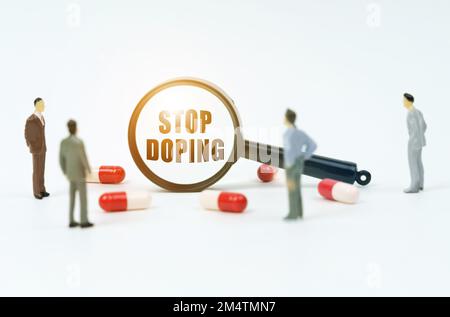 Concetto medico. Su una superficie bianca ci sono pillole, figurine di persone e una lente d'ingrandimento con l'iscrizione - Stop doping Foto Stock